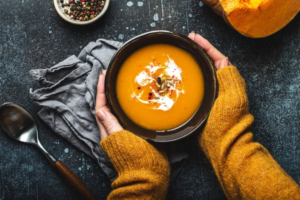 Zwei Hände halten eine wärmende Kürbissuppe