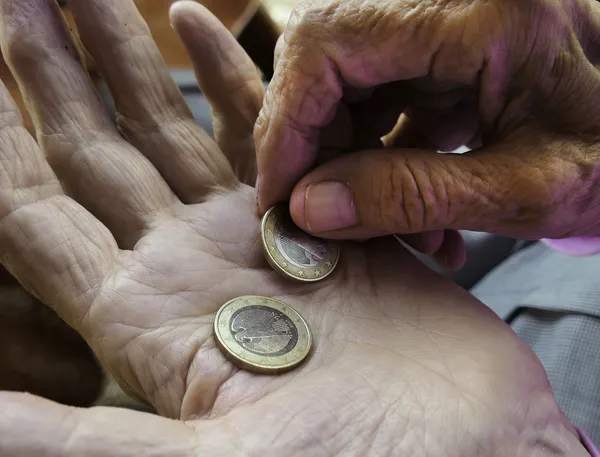 Hand einer älterern Person mit zwei 2-Euro-Münzen