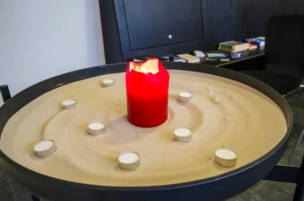 Quelle: Ulli Naefken / uLNaSTUDIOS.com große Schale mit Sand. In der Mitte eine rote Kerze und außenherum Teelichter