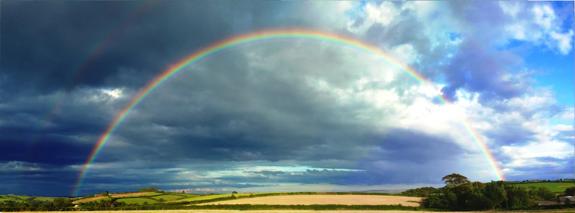 Quelle: PublicDomainPictures/pixabay Regenbogen über Feld bewölkter Himmel