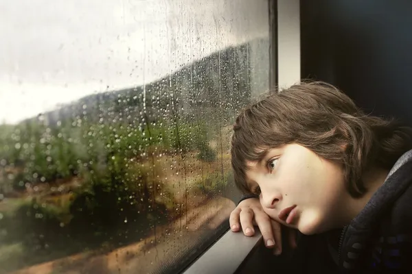 Junge schaut sehnsuchtsvoll aus dem Fenster