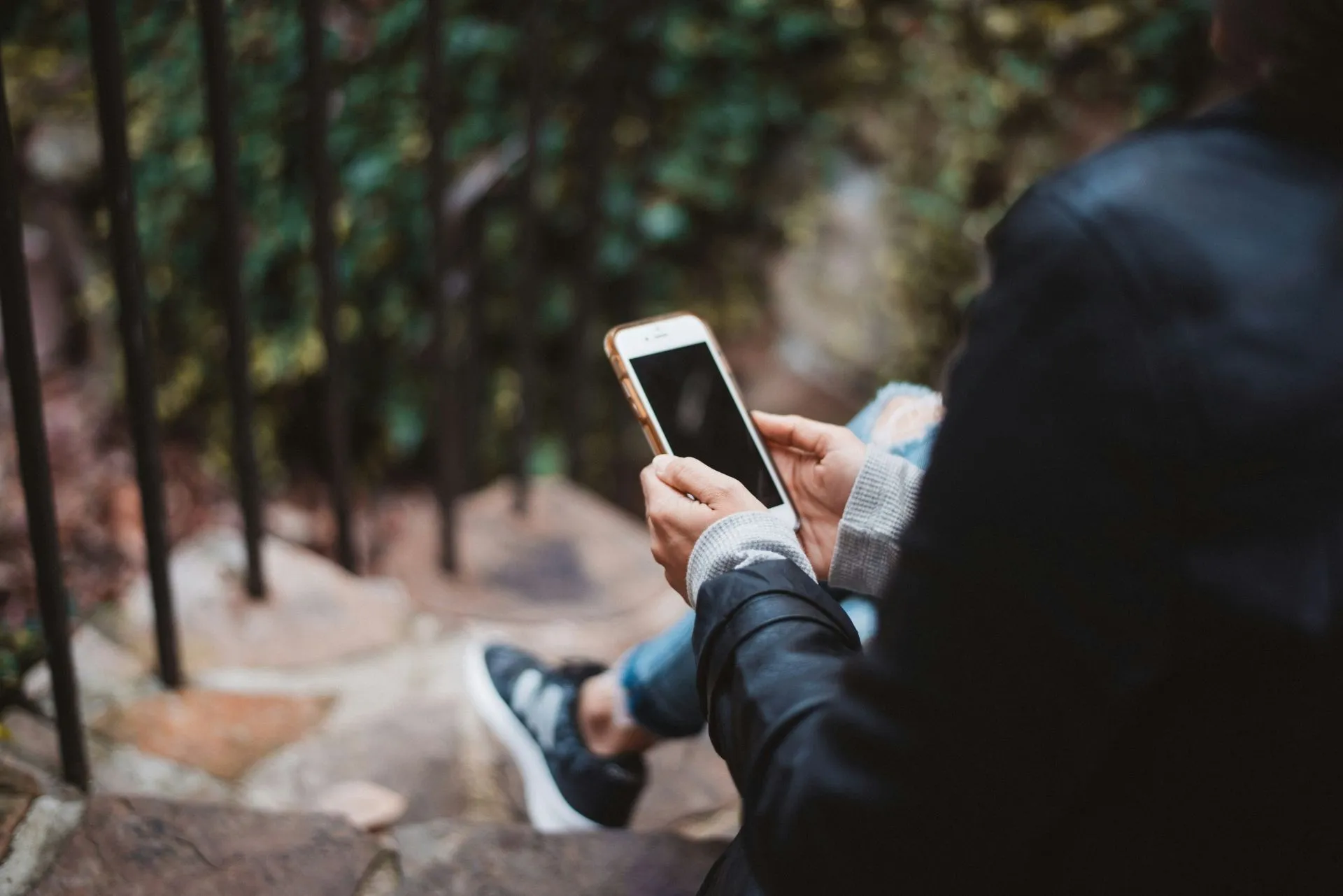 Person mit weißem Smartphone sitzt auf einer Treppe im Freien