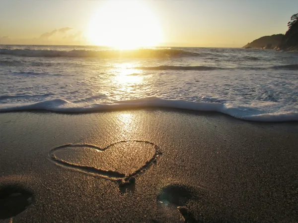 Herz im Sand Meer und Sonne im Hintergrund