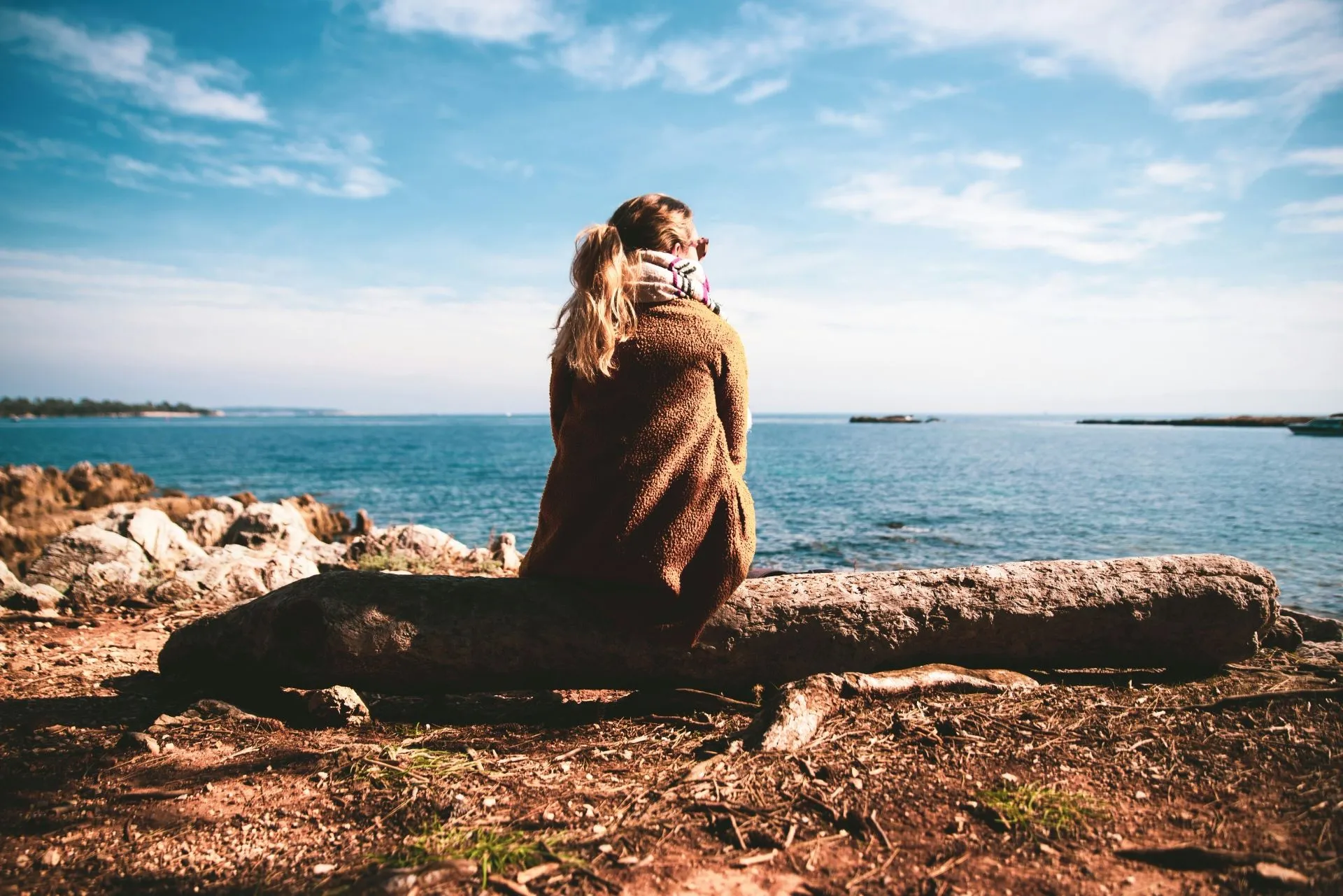 Frau in brauner Jacke blickt auf das Meer