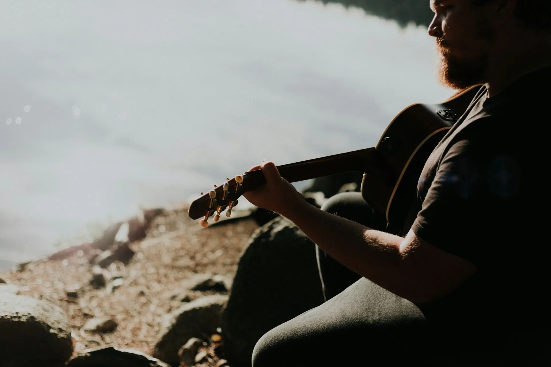 Mann sitzt am Ufer und spielt Gitarre