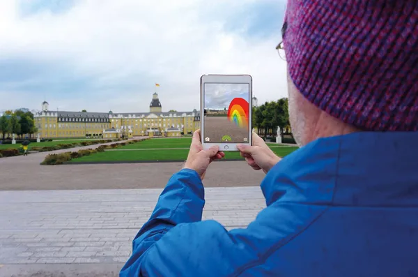 Quelle: Martina Bocher Eine Person setzt mit ihrem iPad einen virtuellen Regenbogen vor das Karlsruher Schloss.