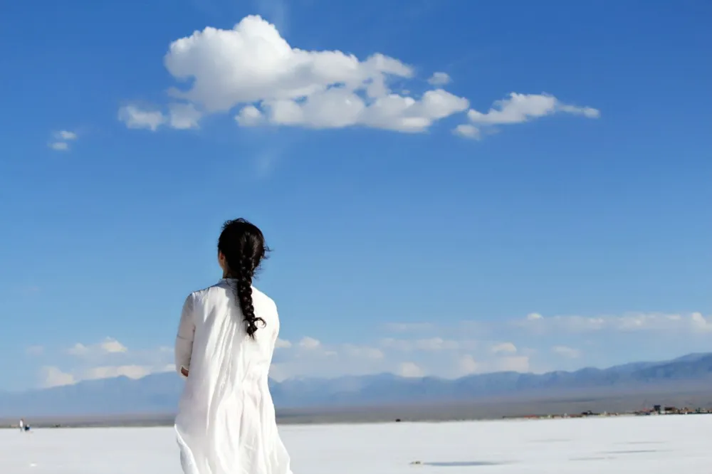 Quelle: Qiuyang/Pixabay Mädchen in weißem Kleid steht am Strand und blickt in den Himmel